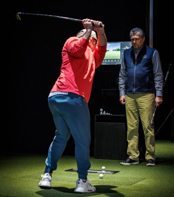 Man practicing his golf swing in front of his instructor